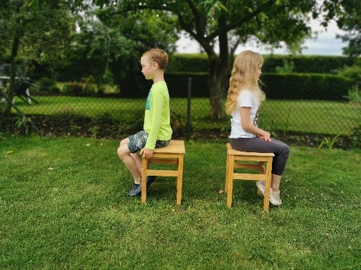 Two children sitting on chairs, with their shoulders back and down, and chins in, demonstrating good posture.