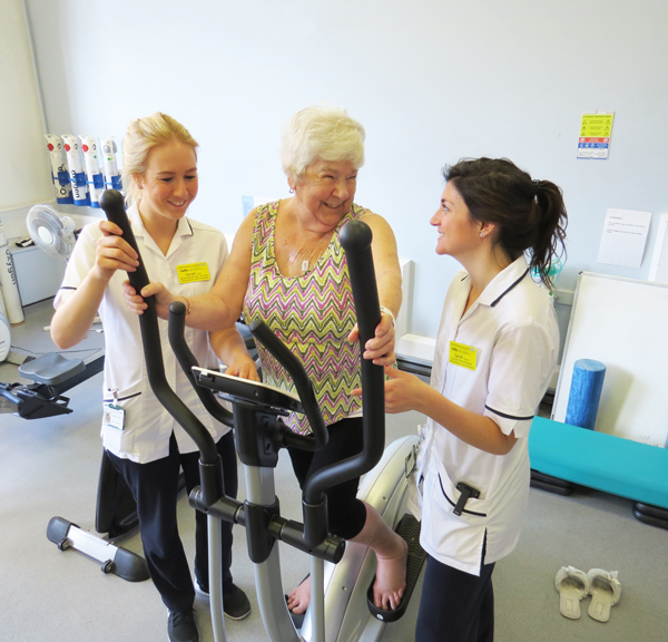 Two physiotherapists working with a patient as she exercises 