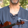 Musician in grey scrubs with a violin in an outdoor setting, with only the bottom half of their face in the frame